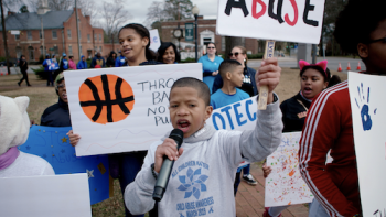 young child at a protest holding a microphone and a sign that says "abuse"